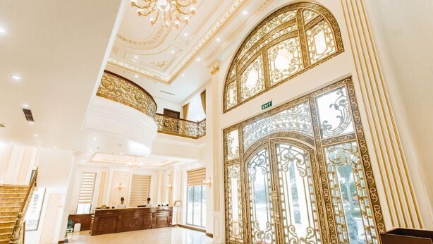 Un lobby lujoso con detalles dorados ornamentales, una recepción y una imponente escalera.