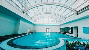 Una piscina interior con diseño curvo, techo de cristal y un mural en la pared.