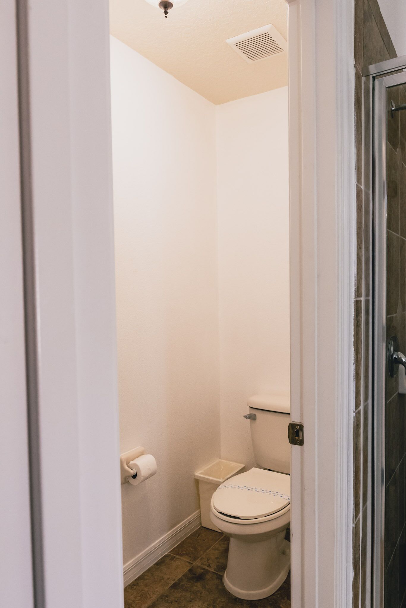 A small, white bathroom with a toilet, a roll of toilet paper, and a shower area.