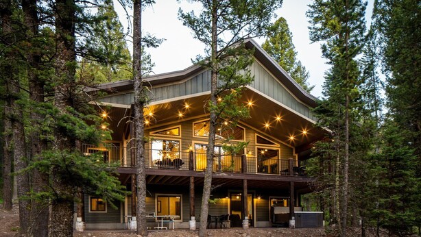 A two-story log cabin with a balcony, surrounded by trees.