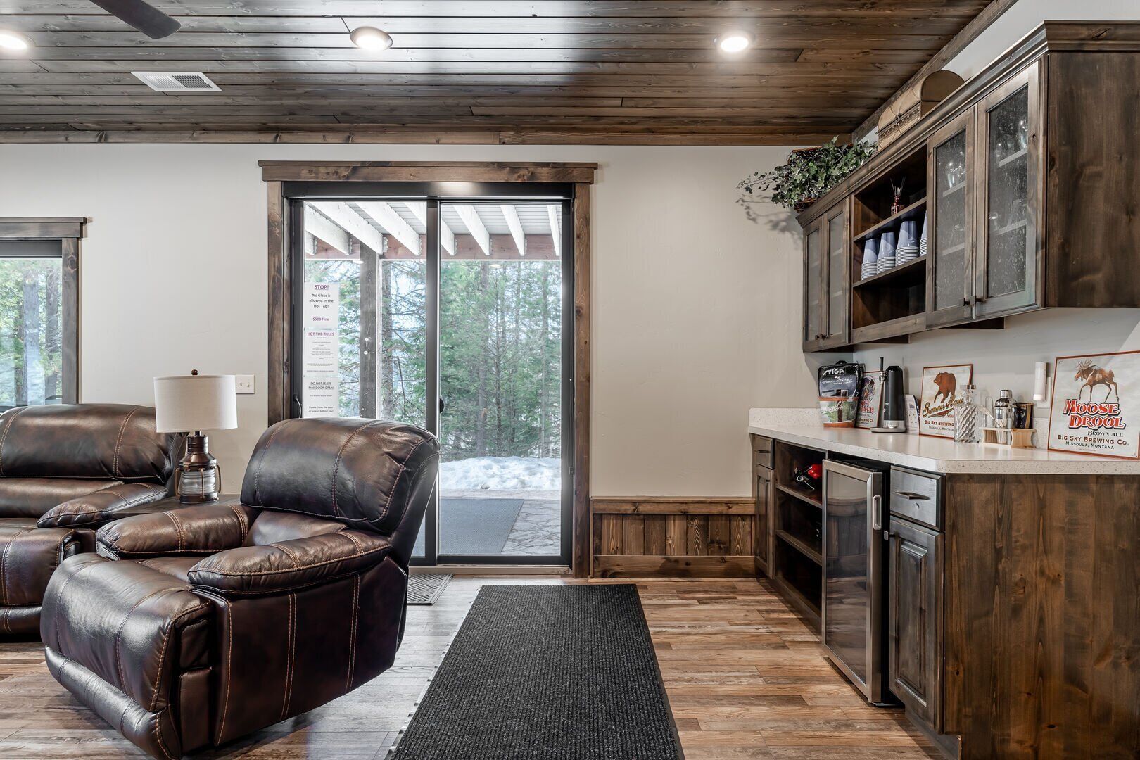 Un espacio de sala acogedor con sillones de cuero, una mesa de centro y una lámpara. Una puerta corrediza de vidrio da a un área exterior nevada.