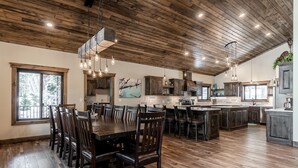 A spacious kitchen with wooden floors, a dining area with a large table and chairs, and a view through a window.