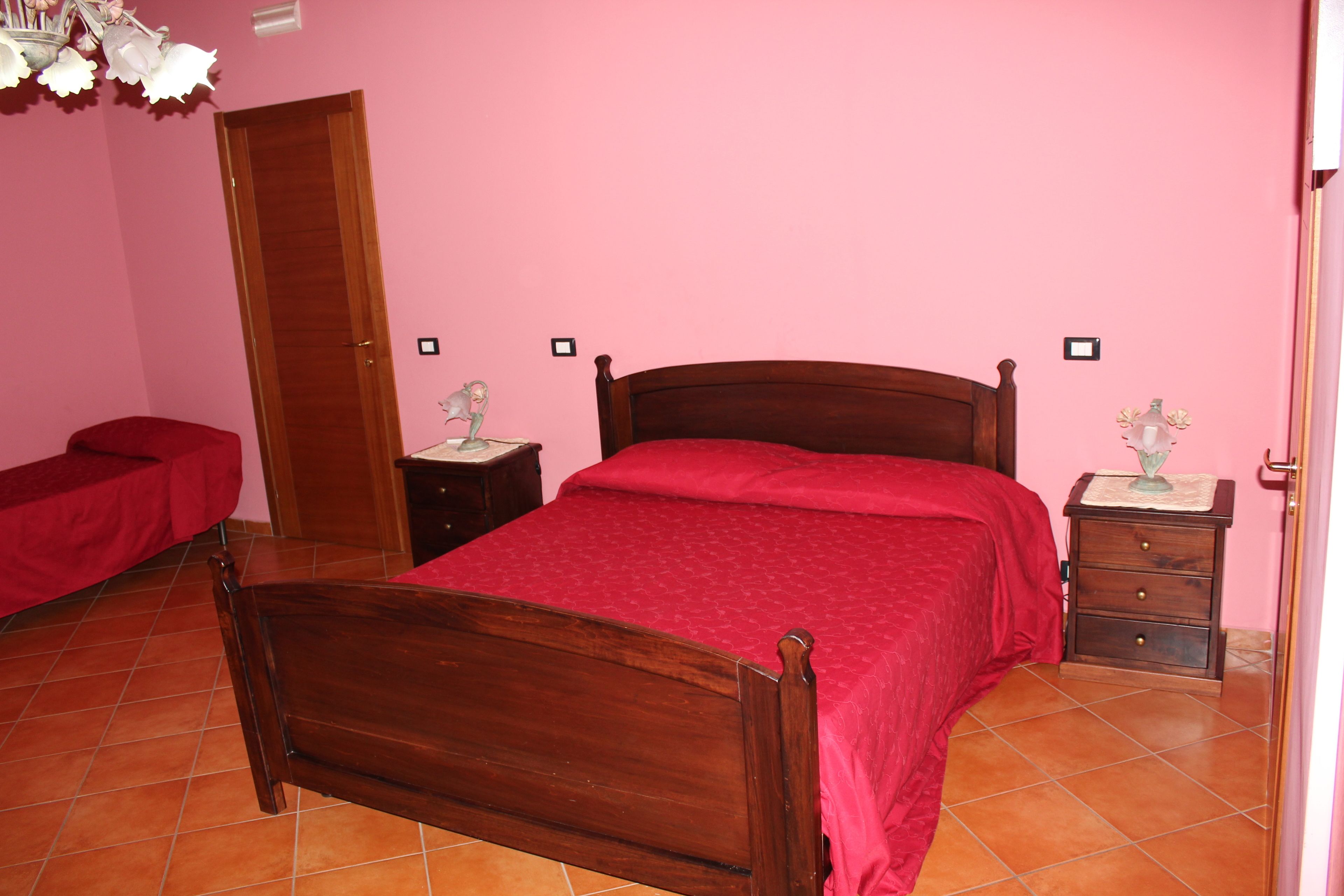 A bedroom with a wooden bed, a red bedspread, a nightstand with a lamp, and a red bench.