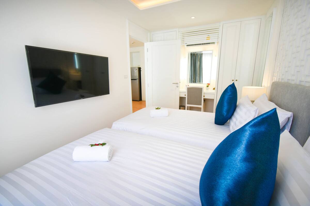 A hotel room with two beds, a TV, a desk, and a mirror.