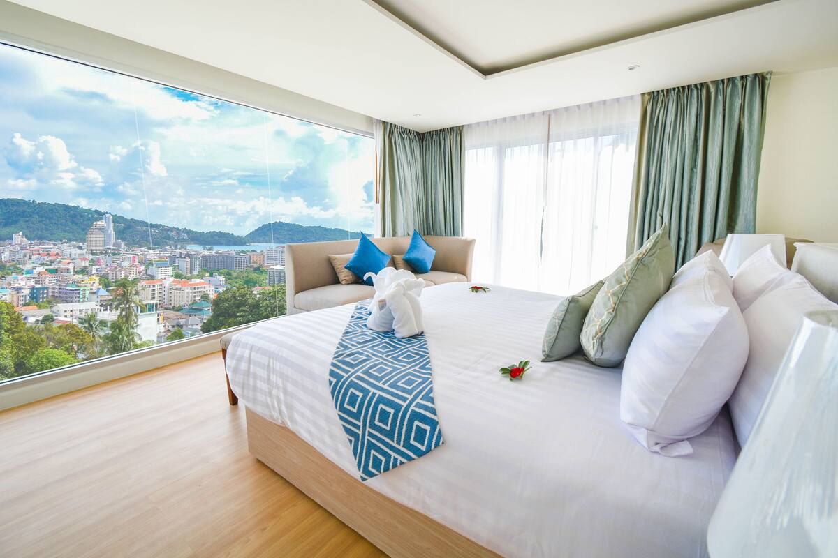 A hotel room with a large bed, a view of a cityscape, and a balcony.