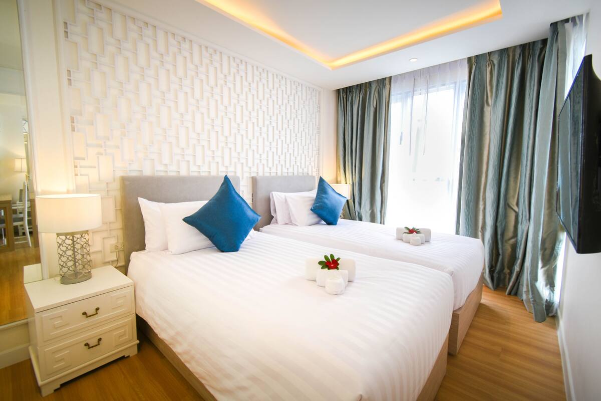 A hotel room with two beds, a nightstand, a lamp, and a decorative wall panel.