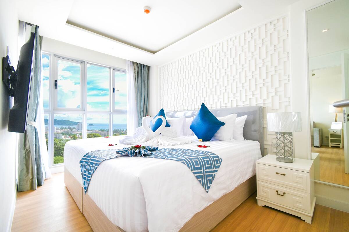 A modern hotel room with a large bed, a nightstand, a mirror, and a view of the city.