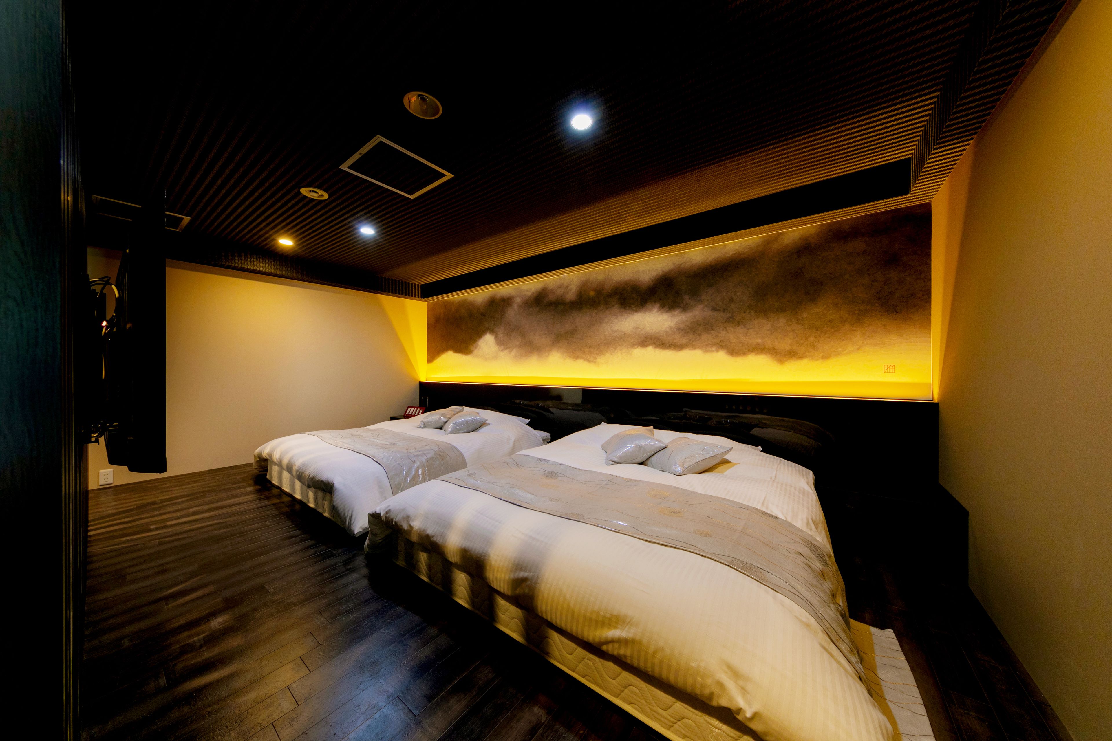 A modern hotel room with a large bed, a headboard with a light panel, and a dark wooden floor.