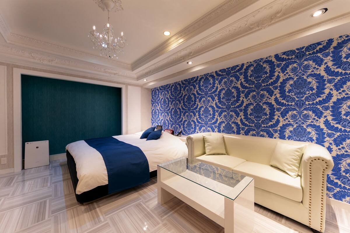 Un dormitorio moderno con una cama grande, una mesita de cristal, un sofá color crema y un papel tapiz estampado en azul.