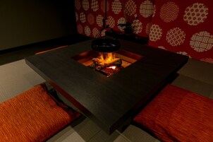 Una habitación moderna con una mesa central que incorpora una chimenea, rodeada de bancos de madera.