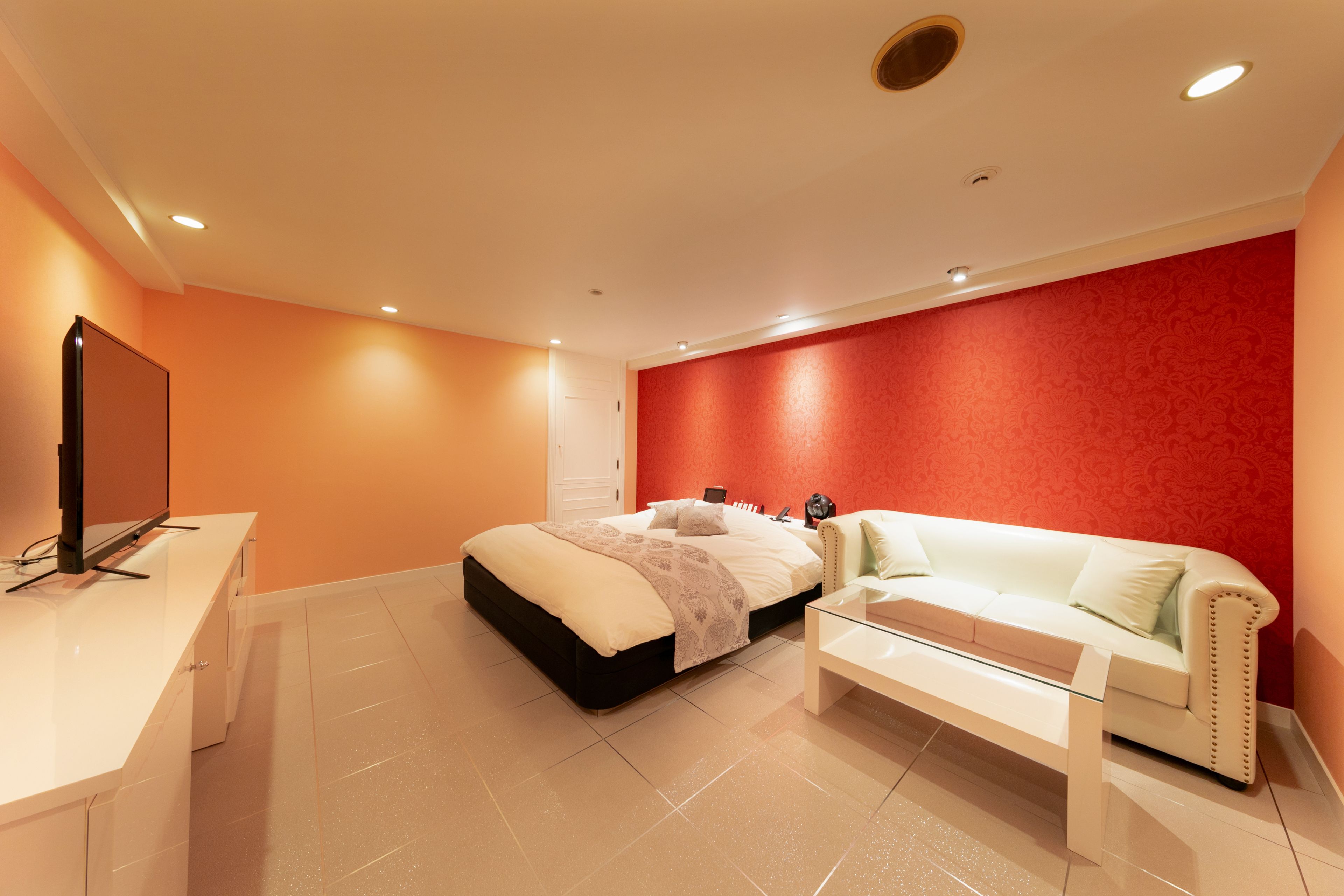 A modern hotel room with a bed, a white sofa, a desk, and a TV.