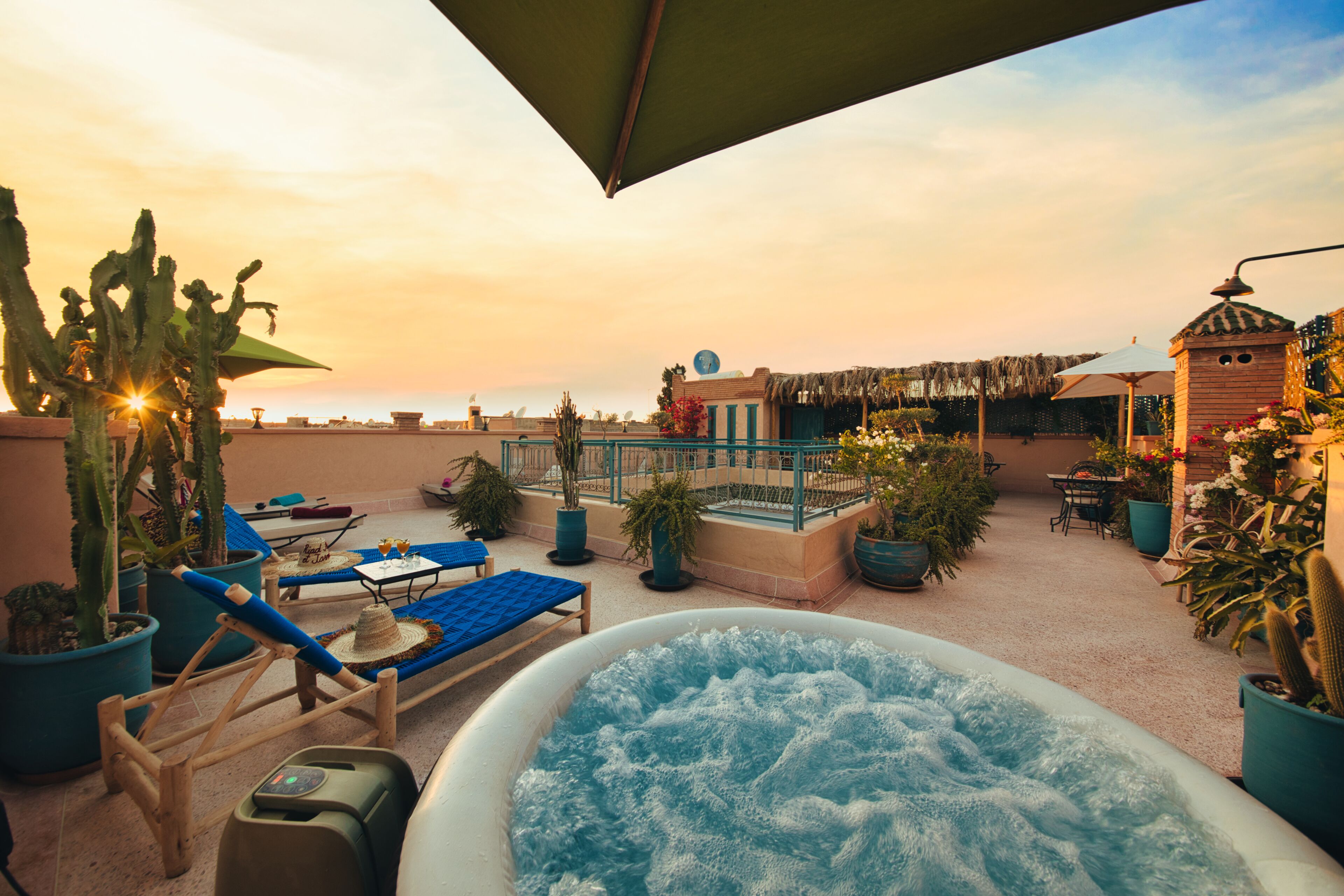 Una terraza en la azotea con jacuzzi, sillones de descanso, plantas en macetas y vistas al atardecer.