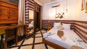 Habitació d'hotel amb escriptori de fusta, llit amb roba de llit blanca, mirall i terra amb rajoles.