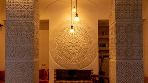 An interior with a large, ornate circular wall design, a fireplace, and a seating area with a red sofa and a chair. - Riad Ambre et Jasmin (Marrakech)