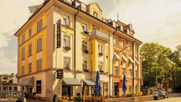 A multi-story hotel with a yellow facade, balconies with flower boxes, and outdoor seating.