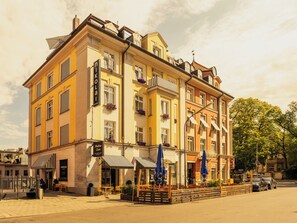 A multi-story hotel with a yellow facade, balconies with flower boxes, and outdoor seating. - Hotel Das Nikolai (Munich)