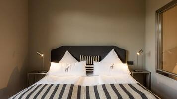 Habitación de hotel con una cama grande, ropa de cama a rayas, dos lámparas de noche y una ventana con vistas.