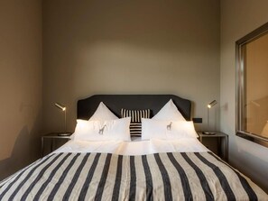 A hotel room with a large bed, striped bedding, two bedside lamps, and a window with a view. - Hotel Das Nikolai (Munich)