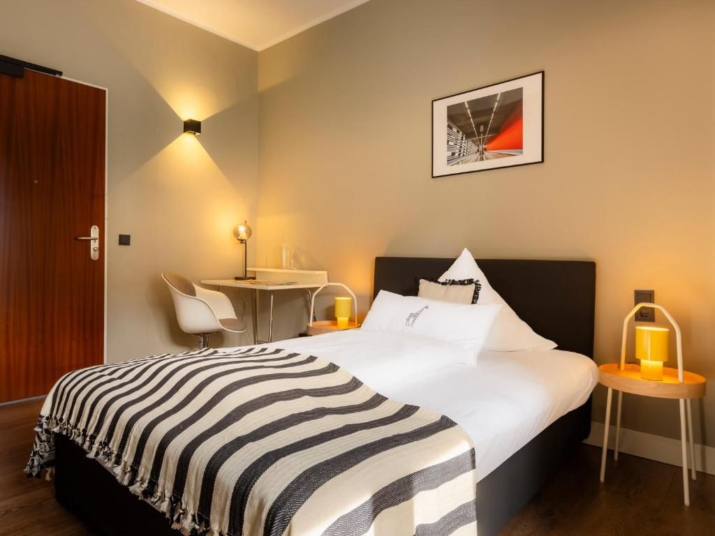 Une chambre d’hôtel comprenant un lit, une table de chevet, une chaise et un bureau avec une lampe.