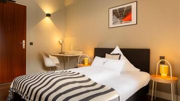 Una habitación de hotel con cama, mesita de noche, silla y escritorio con lámpara.