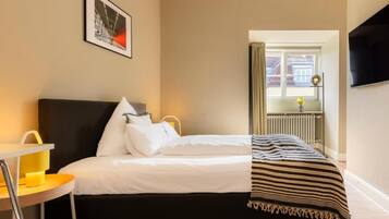 A hotel room with a bed, a chair, a window, and a television.