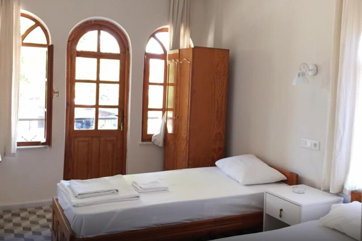 A bedroom with a bed, a wooden wardrobe, and two arched windows with curtains.