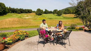 A family dining outdoors with a golf course in the background. - Mountain Lodge At Okemo-1br Fireplace & Updated Kitchen 1 Bedroom Condo by RedAwning (Ludlow)