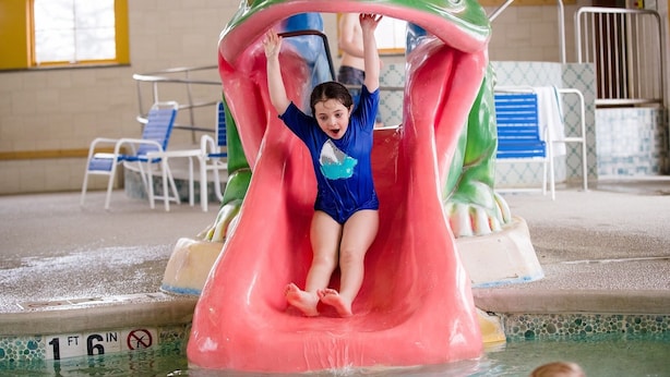 A child sliding down a water slide shaped like a frog, with a pool area in the background. - Mountain Lodge At Okemo-1br Fireplace & Updated Kitchen 1 Bedroom Condo by RedAwning (Ludlow)
