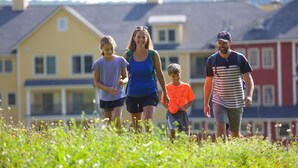 Une famille se promène sur un champ herbeux, avec des maisons en arrière-plan.