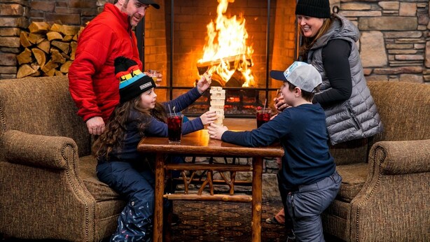 Une famille joue au Jenga devant une cheminée.