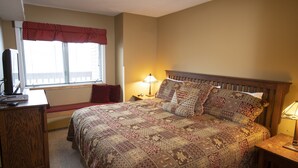 Une chambre à coucher avec un grand lit, un bureau, une chaise, une fenêtre avec des stores et une lampe.