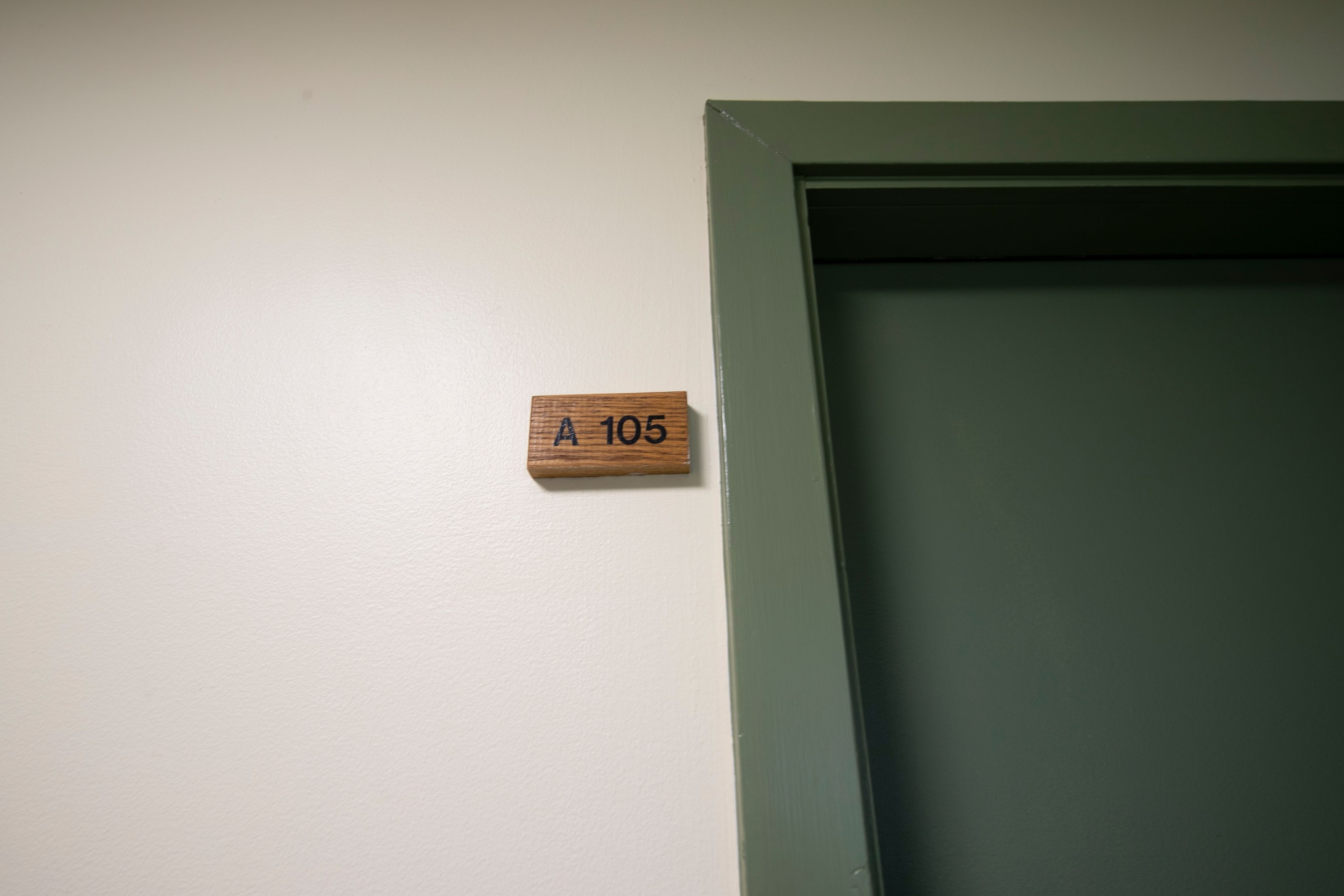 A wooden sign with the number "A 105" on a white wall next to a green door.