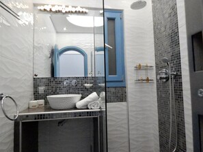 A modern bathroom with a glass shower enclosure, a white sink, and a blue-framed mirror. - Captain Lazaros Villas (Santorini)