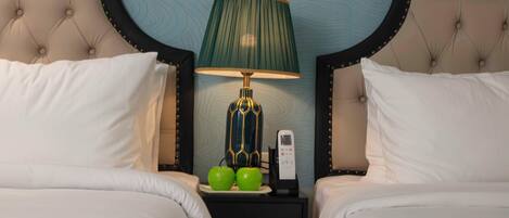 A hotel room with two beds, a nightstand with a lamp, two green apples, and a phone.
