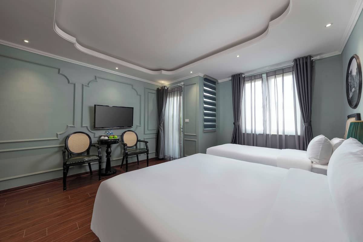 Une chambre d’hôtel avec deux lits, une télévision, une petite table avec des chaises et une fenêtre avec des rideaux.