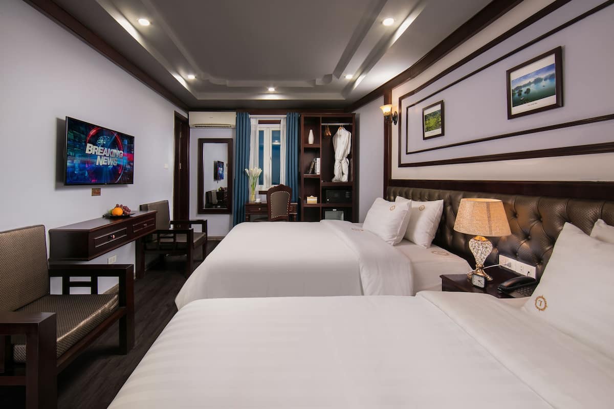 Une chambre d’hôtel avec deux lits, une télévision, un bureau, une chaise, une armoire et une salle de bain visible à travers une porte ouverte.