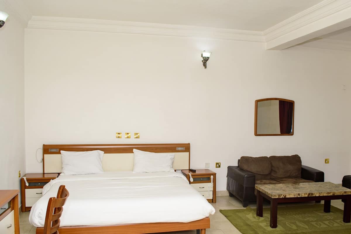 A hotel room with a large bed, a wooden nightstand, a brown sofa, a small table, and a green rug.