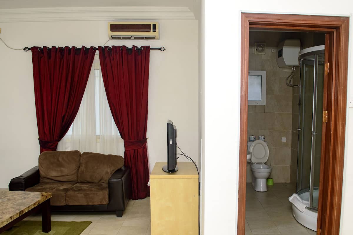 A living room with a sofa, a television on a stand, and a window with red curtains.