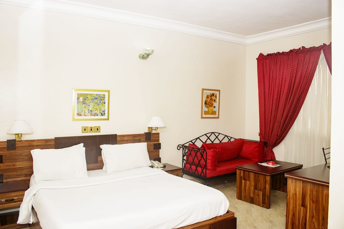 A hotel room with a large bed, a red sofa, two wooden nightstands, and a small table.