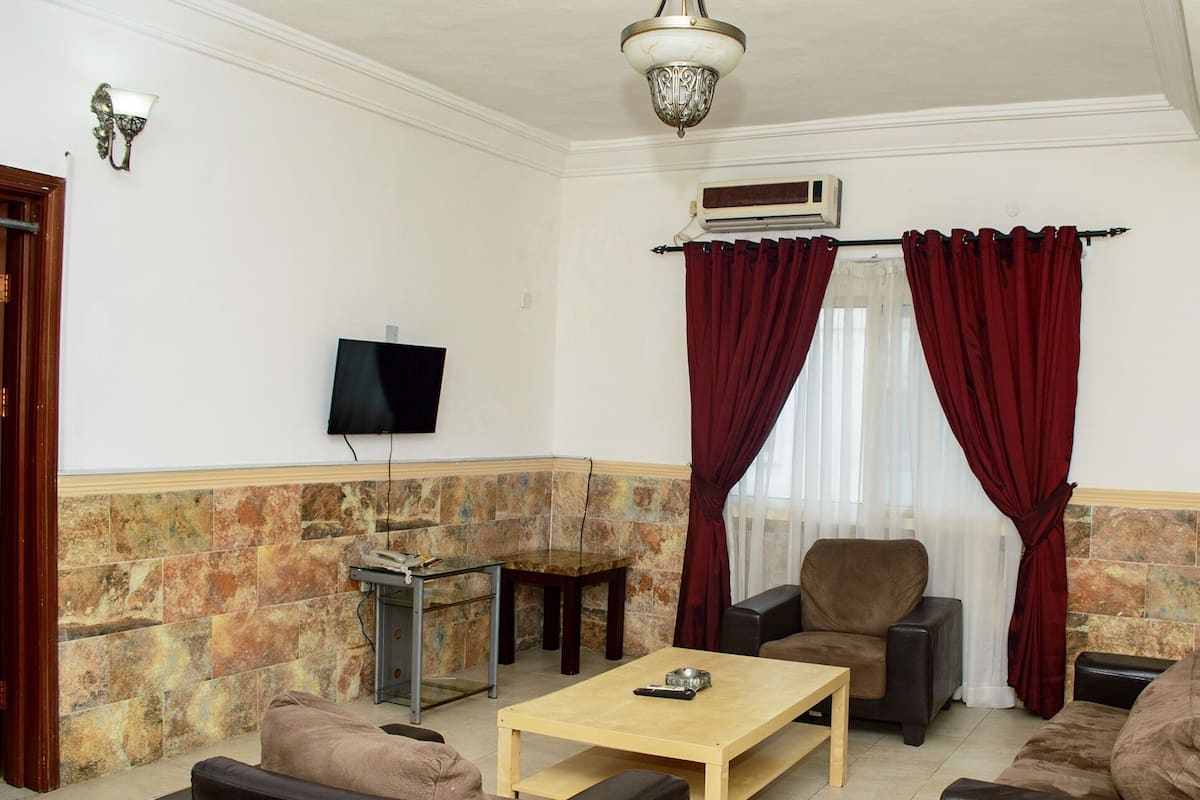 A living room with a flat-screen TV, a fireplace, a sofa, a coffee table, and red curtains.