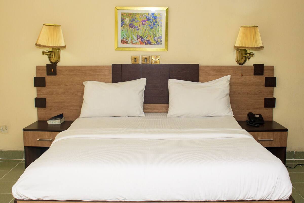 A hotel room with a large bed, two bedside tables, a nightstand with a phone, and wall-mounted lamps.