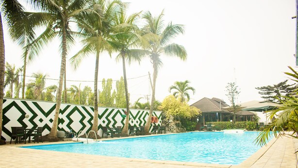 A swimming pool with a chevron-patterned wall, palm trees, and outdoor seating. - Bougainvillea Hotel (Port Harcourt)