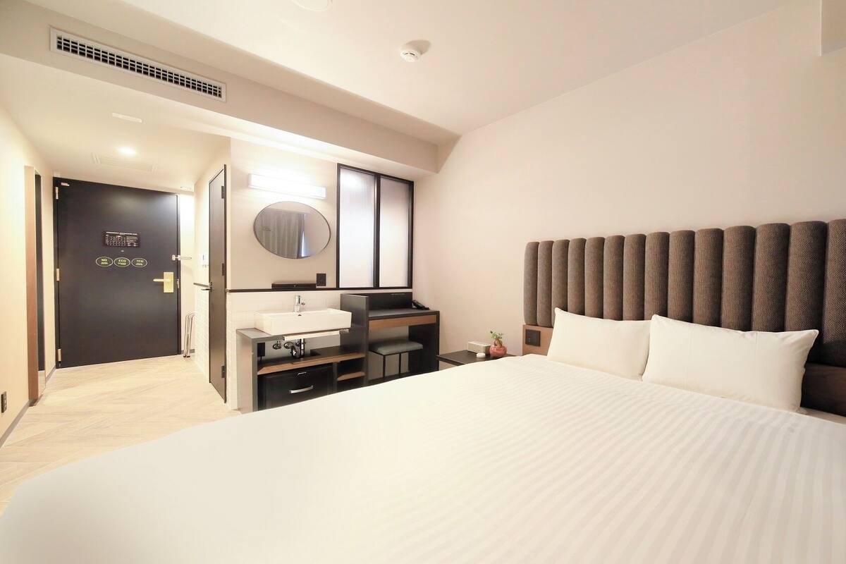 A hotel room with a large bed, a bedside table, a mirror, a built-in desk with a sink, and a headboard.