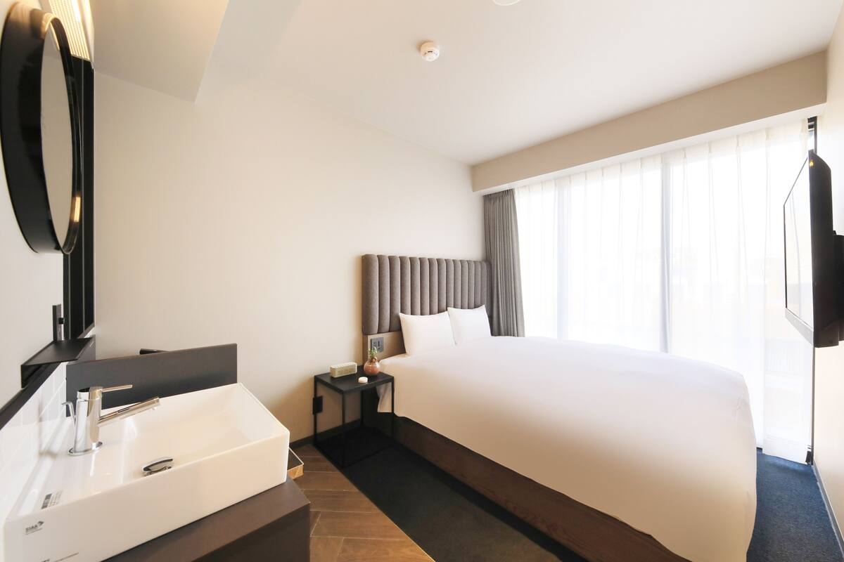 A hotel room with a large bed, a modern bathroom with a large sink, and a flat-screen TV mounted on the wall.
