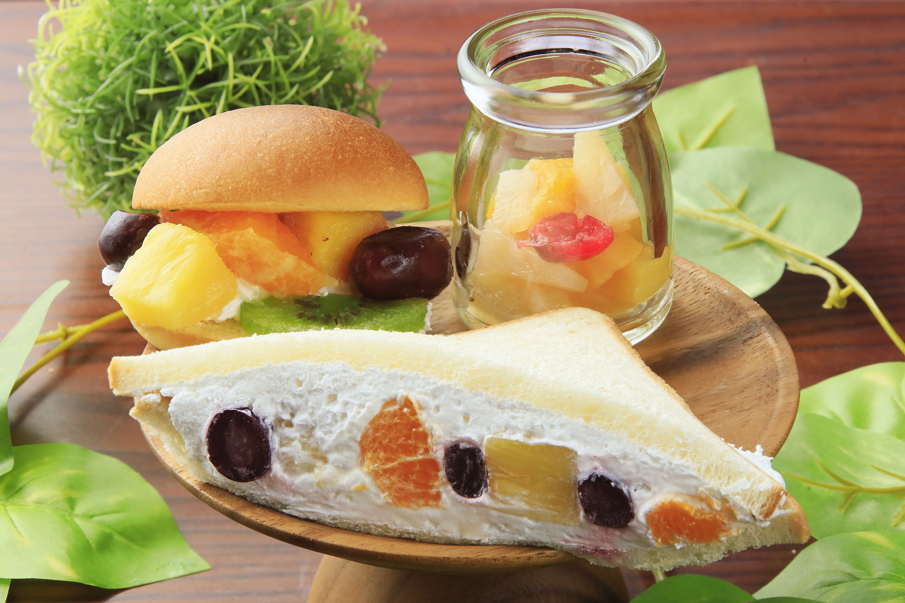 A sandwich with fruit and a glass jar of fruit salad on a wooden board.