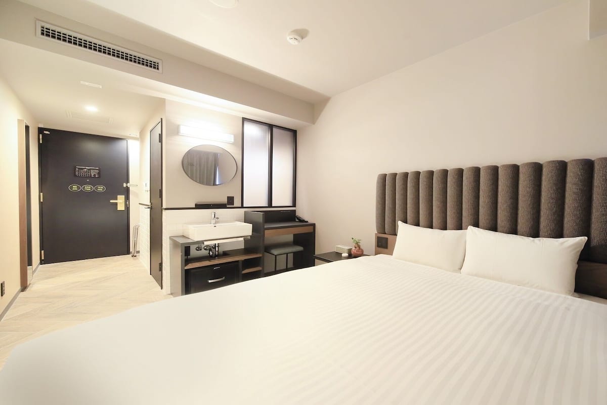 A hotel room with a large bed, a vanity with a mirror, a desk, and a headboard with vertical panels.