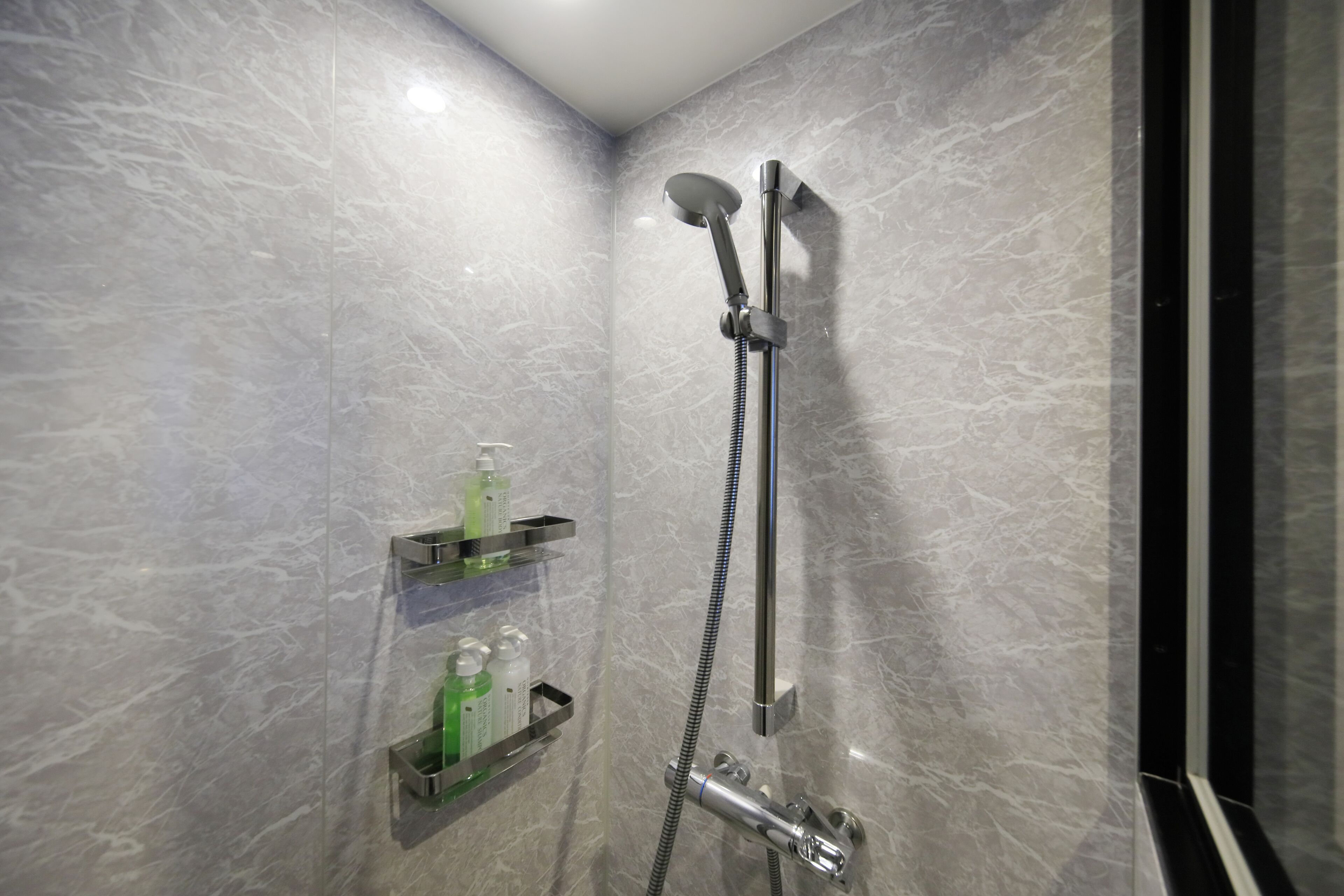 Une salle de bain moderne avec une douche, des murs en marbre et une étagère contenant des articles de toilette.
