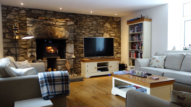 A cozy living room with a stone fireplace, a flat-screen TV, a bookshelf, and comfortable seating.