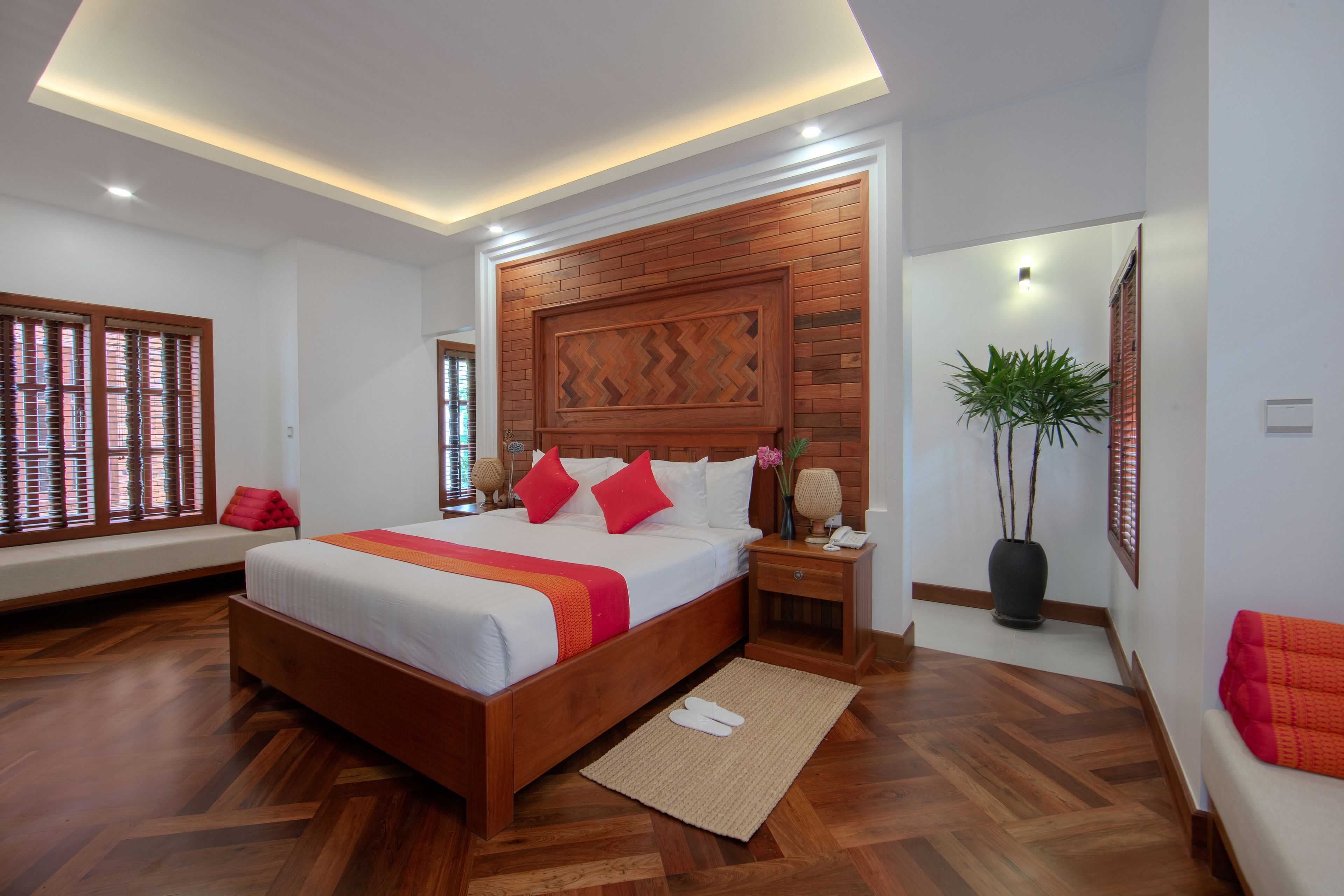 A modern hotel room with a large bed, wooden headboard, and a potted plant.