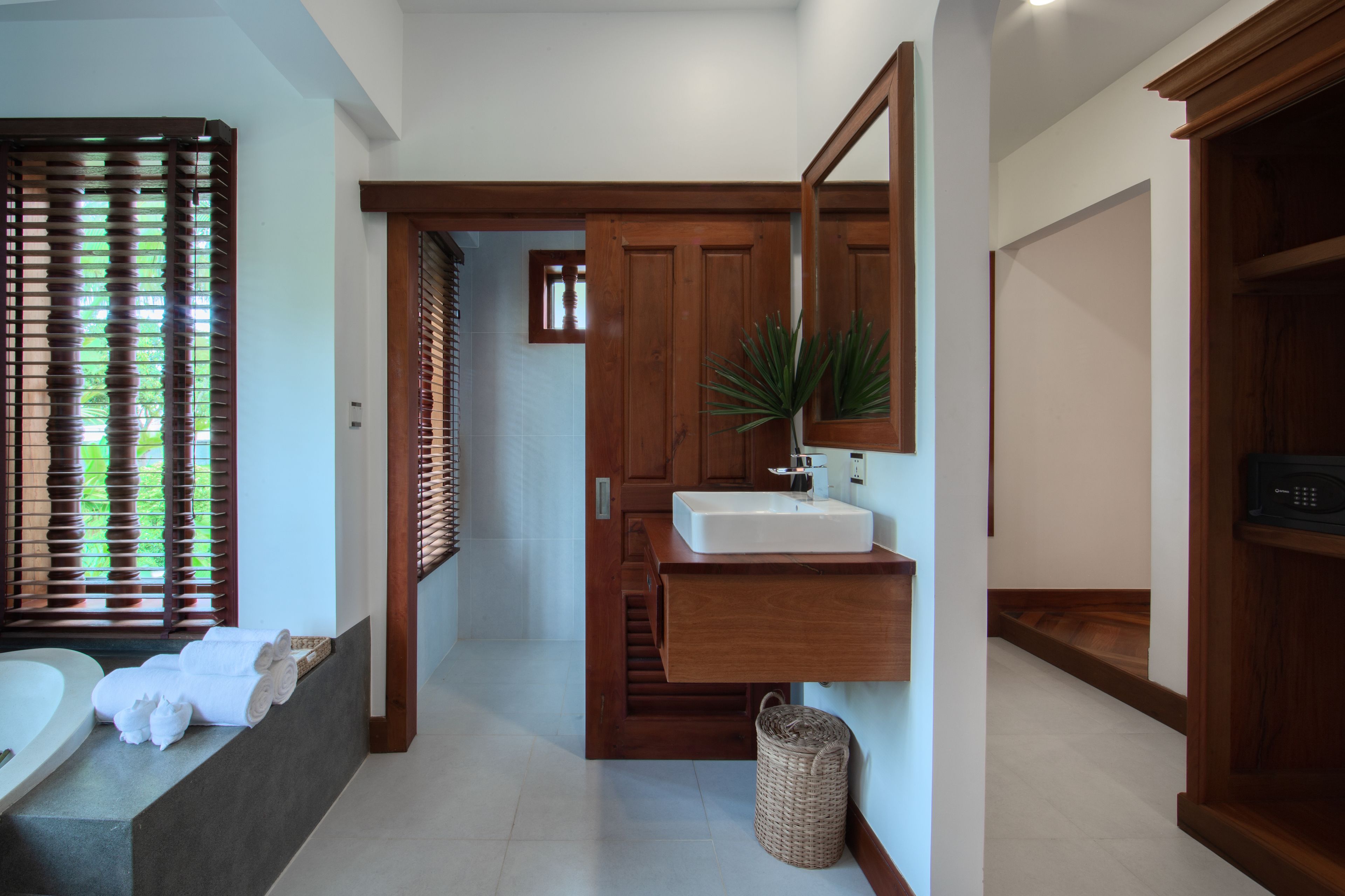 A modern bathroom with a bathtub, a sink, and a mirror. There is a plant on the sink counter and a basket on the floor.